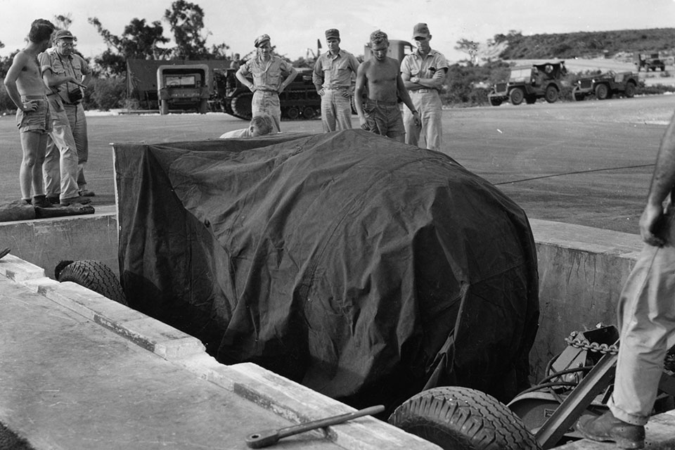 Covered for security, "Fat Man" is lowered into the pit where it can be loaded into the bomber. National Archives)