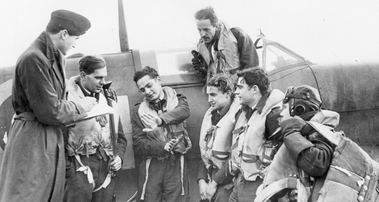 The Intelligence Officer at the headquarters of the second Eagle Squdron (121 Squadron), Sir Michael Duff-Assheton-Smith, takes notes as pilots describe their most recent sortie. They are, (L to R) Sq. Ldr. Powell; Pilot Officers W. James Daly, Hugh Kennard, Le Roy A. Skinner, Clarence Martin, and (standing on wing), R. Fuller Patterson.