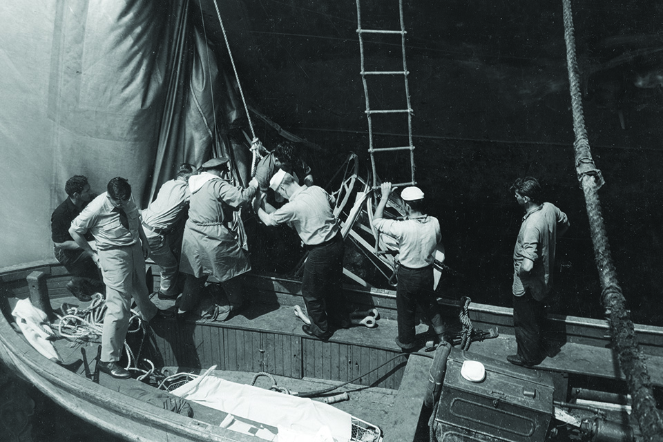 Sailors help one of the surviving crewmen onto a motor launch. (National Archives)