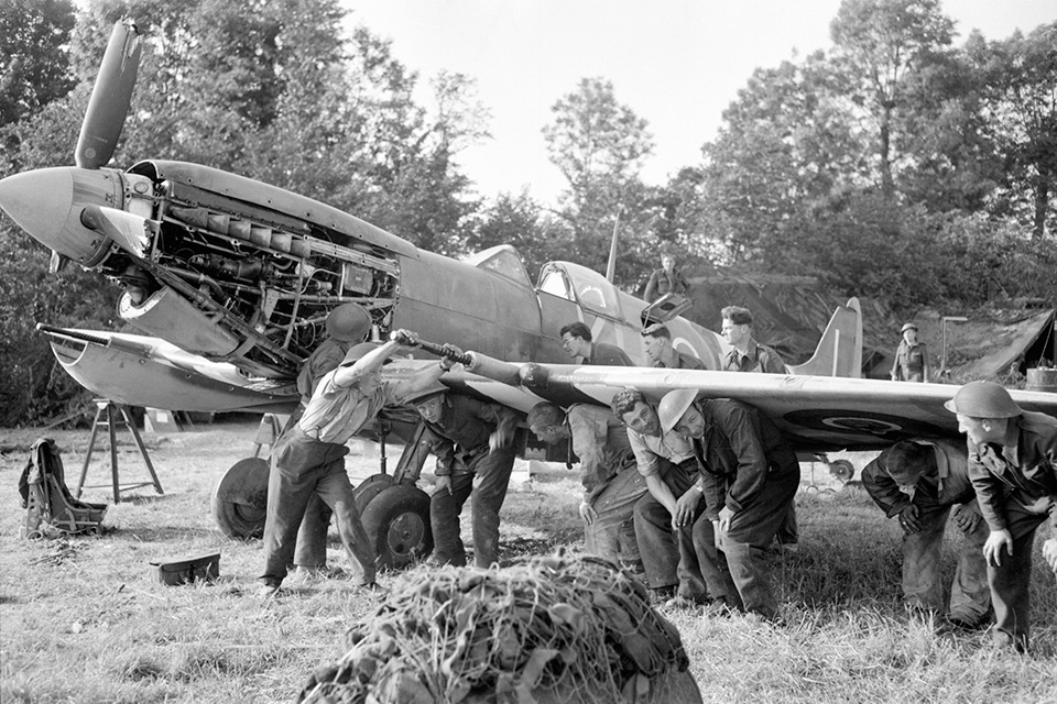 Repairmen put their backs into their work as they manhandle a damaged Spitfire Mk. IX at a forward airfield in Normandy in June 1944. (IWM CL 0186)