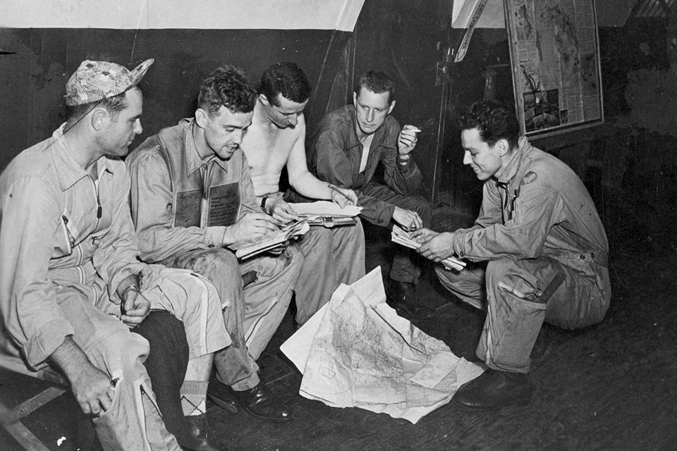 The two Twin Mustang crews surround a shirtless intel officer, recounting the day's action. From left: pilot Moran, 1st Lt. Fred Larkins, unidentified, pilot Hudson and Fraser. (U.S. Air Force)