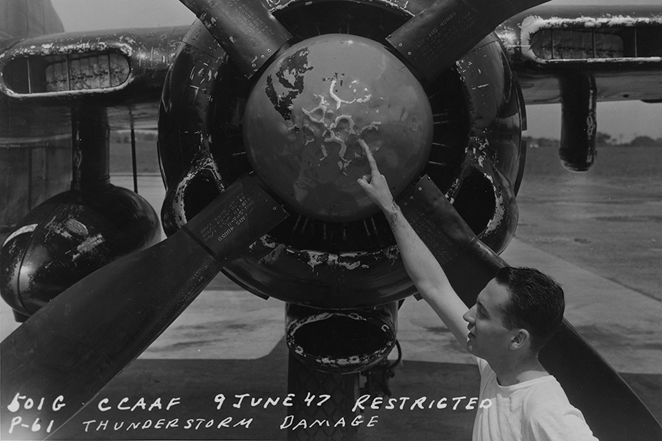 A ground crewman points to spinner damage sustained by a Black Widow while flying through a thunderstorm in June 1947. (National Archives)