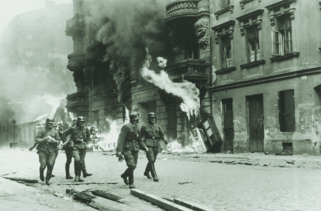 SS troops walk past a block of burning buildings in the Warsaw ghetto; the original German caption reads, simply: “An assault squad.” (U.S. Holocaust Memorial Museum, Courtesy of National Archives and Records Administration, College Park)