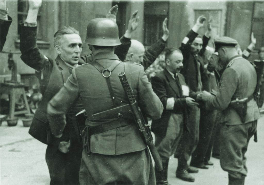 SS troops and police search Jewish department heads at an armaments factory in Warsaw (above); other ghetto residents line up against a wall before a weapons search (below). Many thousands were deported to death or labor camps. (U.S. Holocaust Memorial Museum, Courtesy of National Archives and Records Administration, College Park)