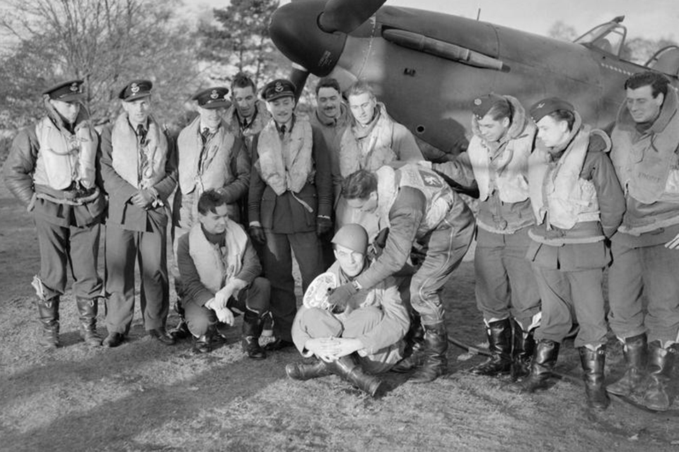 Royal Air Force Squadron Leader Robert Stanford Tuck poses with a group of 257 Squadron pilots under the nose of Tuck's Hawker Hurricane. They are displaying souvenirs of their action against Italian aircraft on November 11, 1940. (IWM CH1647)