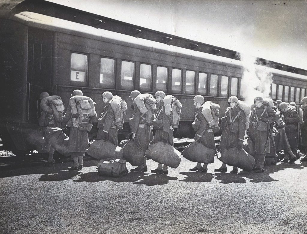 Duffle bags in tow, soldiers board a train south to waiting transport ships.