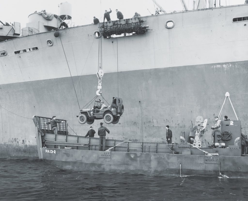 A jeep is lowered onto Jack Rowe’s LCM (Landing Craft, Mechanized) during final invasion training. Rowe is leaning against the ramp at the far left. (U.S. Coast Guard Collection/National Archives)