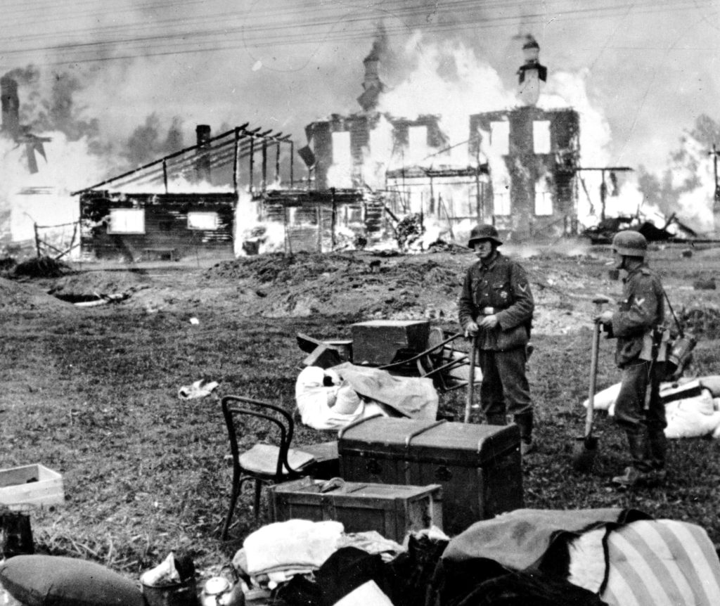 German soldiers, surrounded by plundered furniture, smoke cigarettes while a church and a home burn during the Siege of Leningrad in 1941. / Polish State Archive
