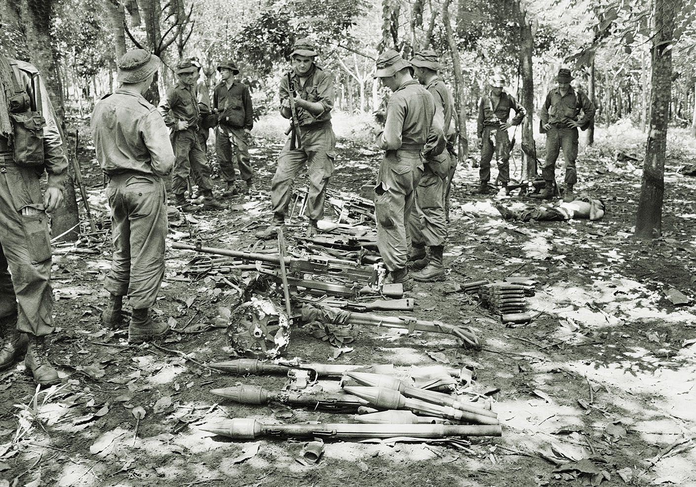 After the battle, troops in the rubber plantation examine Viet Cong weapons, including rocket launchers, heavy machine guns and recoilless rifles. / Australian War Memorial