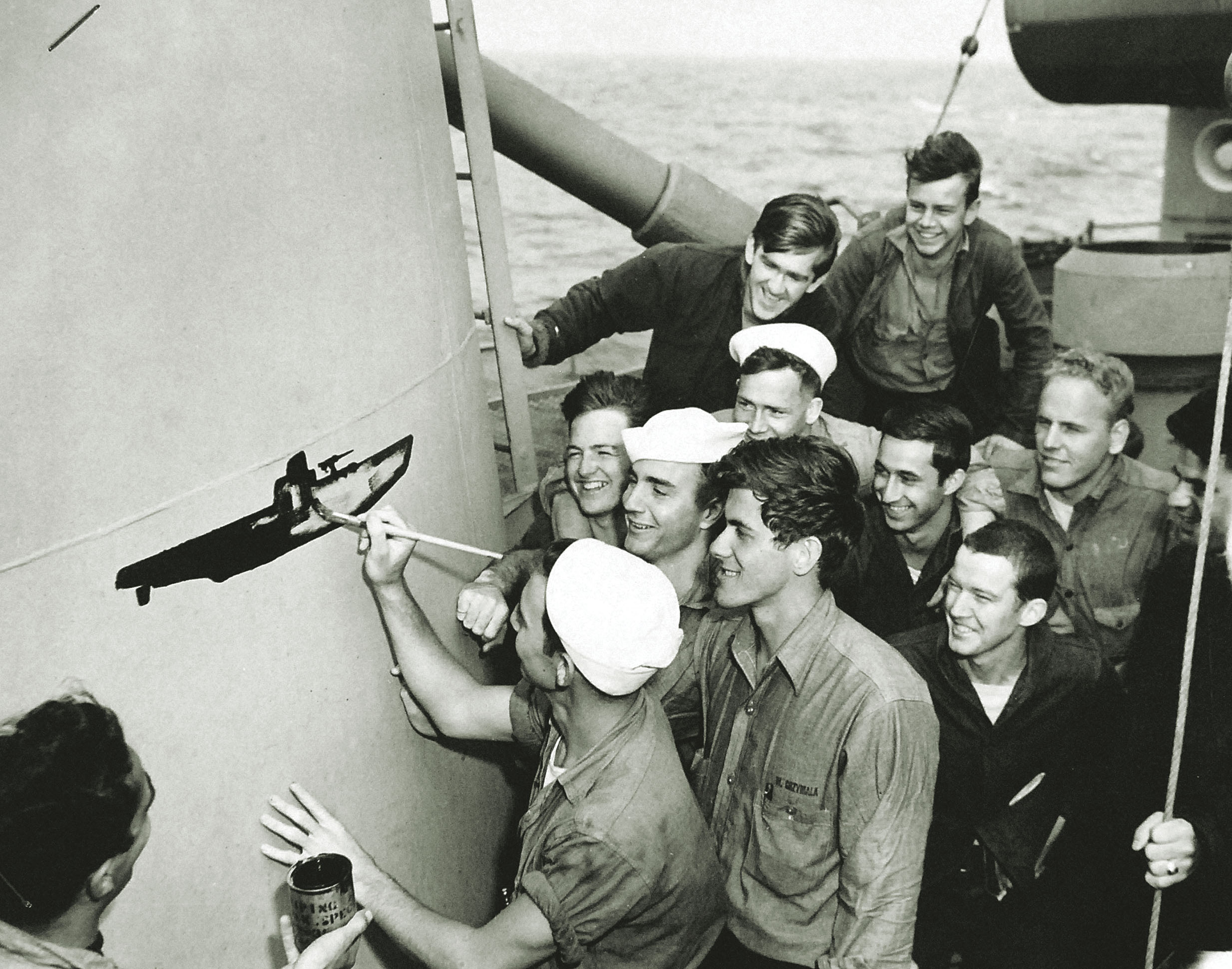 Jubilant over the sinking of U-853, Moberly’s Coast Guard Reserve crew gathers to watch a crewmate paint a victory symbol on the frigate’s funnel. / U.S. Coast Guard