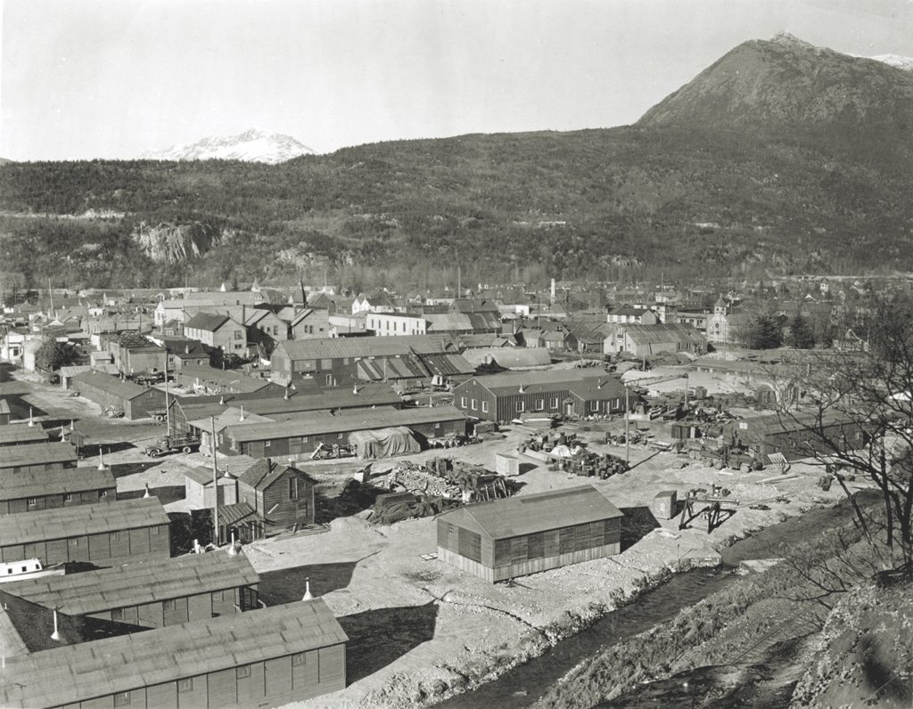 During the war years, Skagway (top, circa 1943) saw another boom as the town swelled to make room for an influx of G.I.s. The war materiel they hauled north arrived at Skagway via its port (below)—where a freighter in the foreground unloads a shipment of coal. (Courtesy of Jerry Latham) 