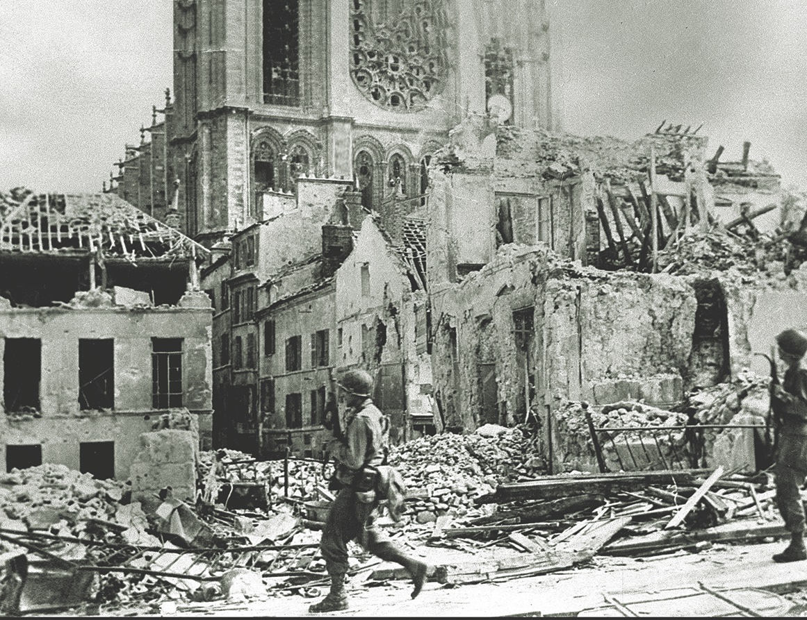 Two soldiers from the 79th Division pass Mantes-Gassicourt’s bombed-out cathedral. (USIS-DITE/Bridgeman Images) 