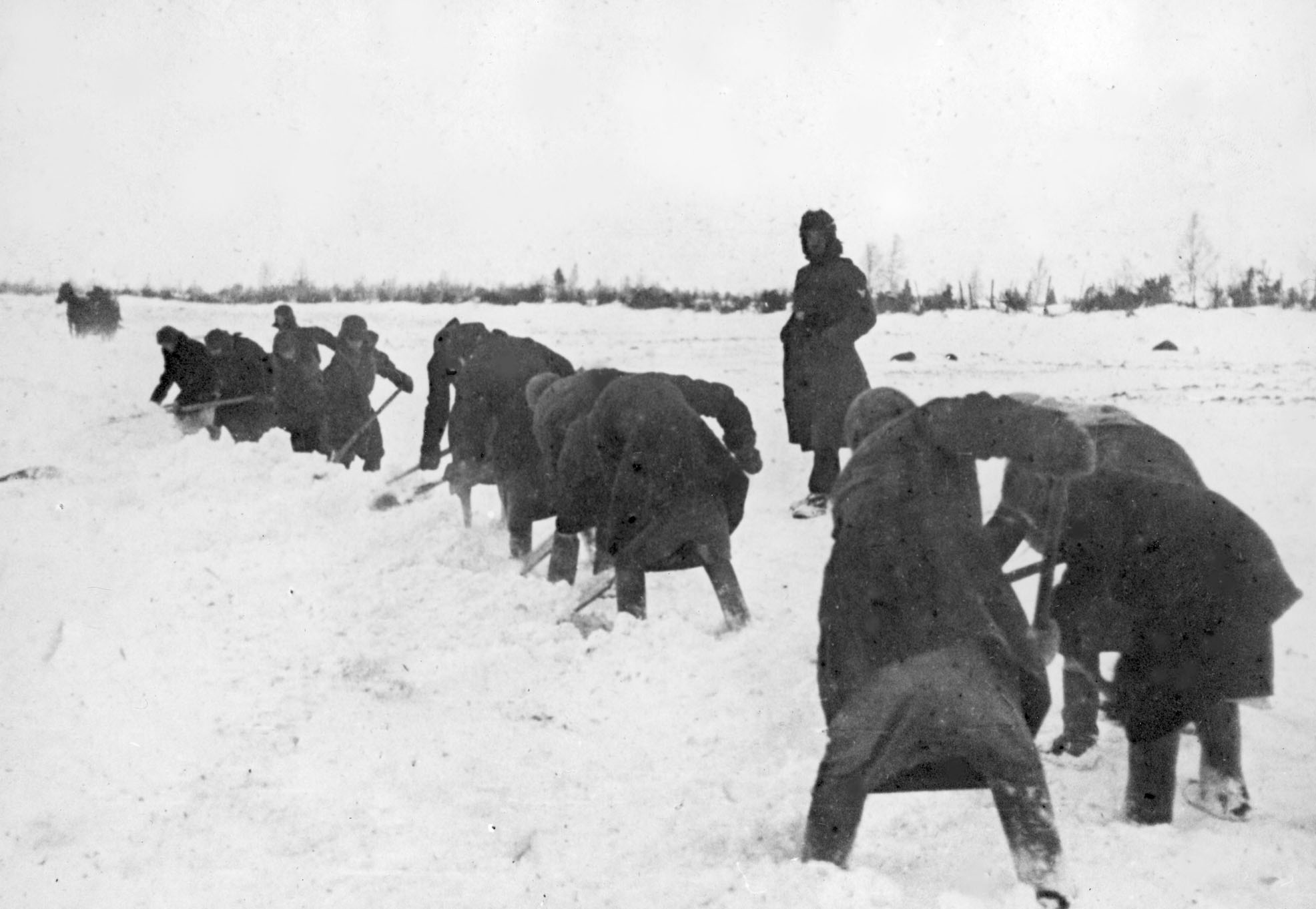 A German overseer guards Soviet prisoners as they are forced to perform manual labor, while being deprived of food, water and shelter, circa 1941. / Polish State Archive