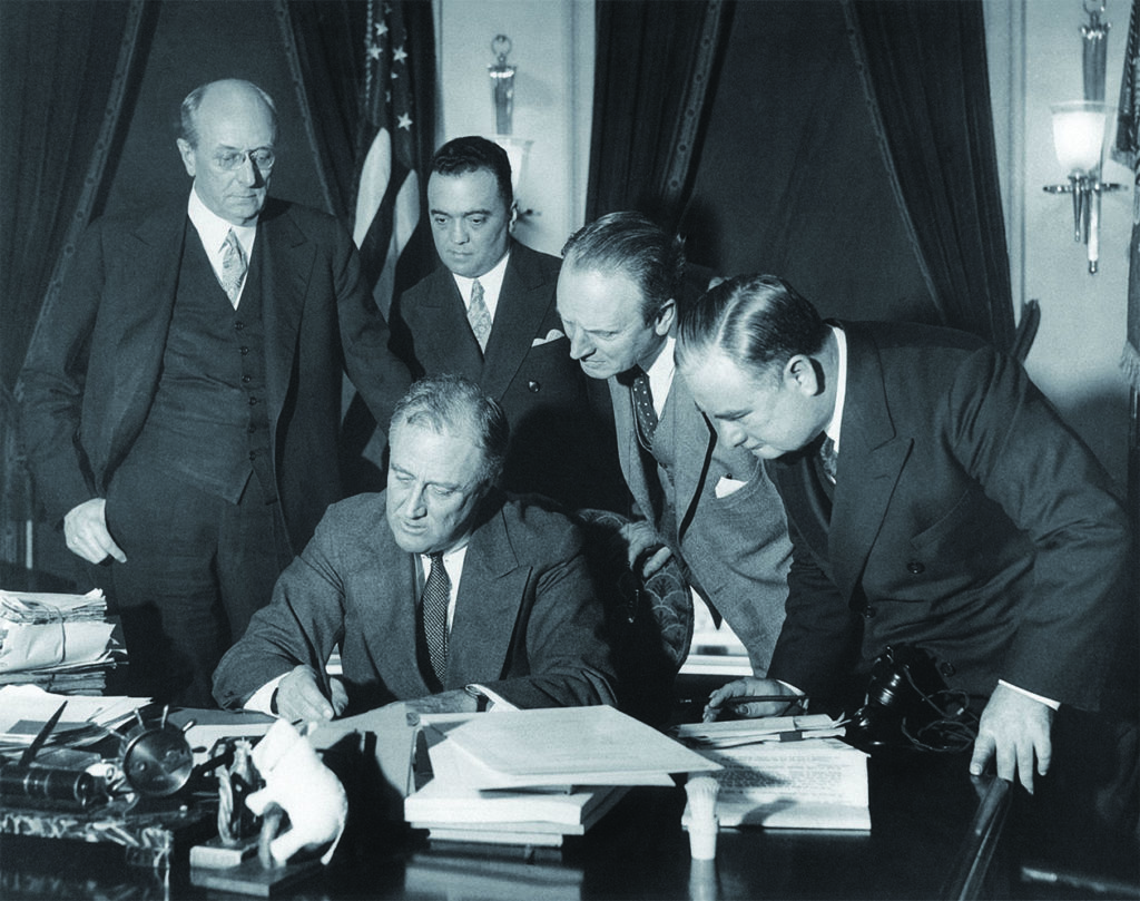 President Roosevelt signs the 1934 crime bill into law. Looking on from left: Attorney General Homer Cummings; J. Edgar Hoover, director of the Division of Investigation; unidentified; Assistant Attorney General Joseph Keenan. (Everett Collection/Alamy Stock Photo)
