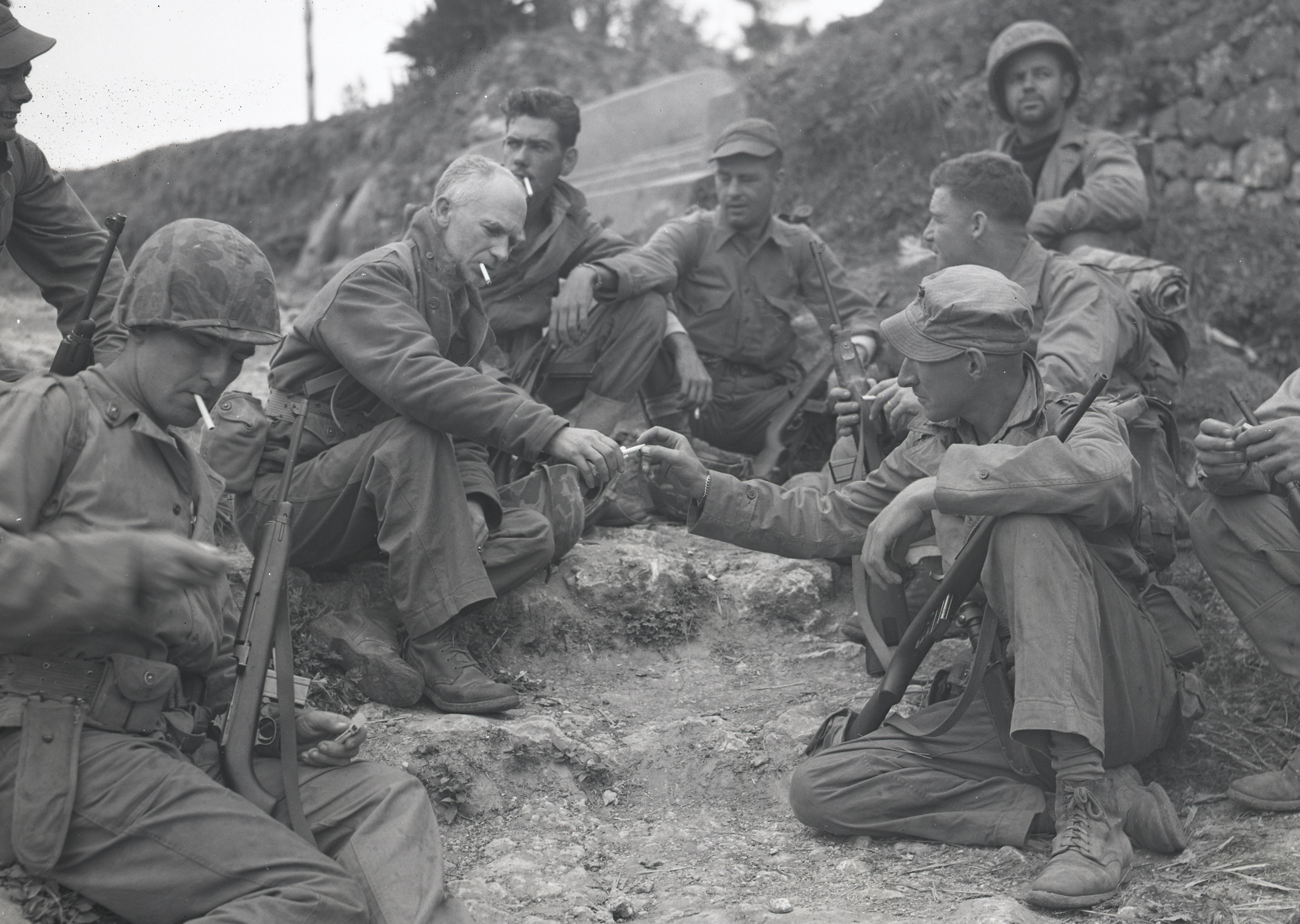 Ernie Pyle (center left) shares cigarettes with U.S. Marines by a roadside on Okinawa on April 8, 1945, not long before his death. / U.S. National Archives