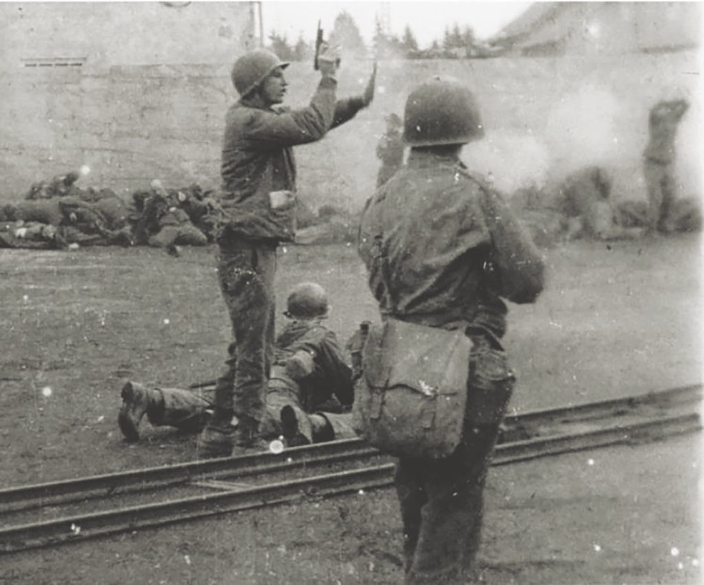 Lt. Col. Felix L. Sparks raises his pistol in an effort to stop the shooting. His sympathies, though, remained with the troops: “Dante’s ‘Inferno’ seemed pale compared to the real hell of Dachau,” he later wrote. (National Archives)