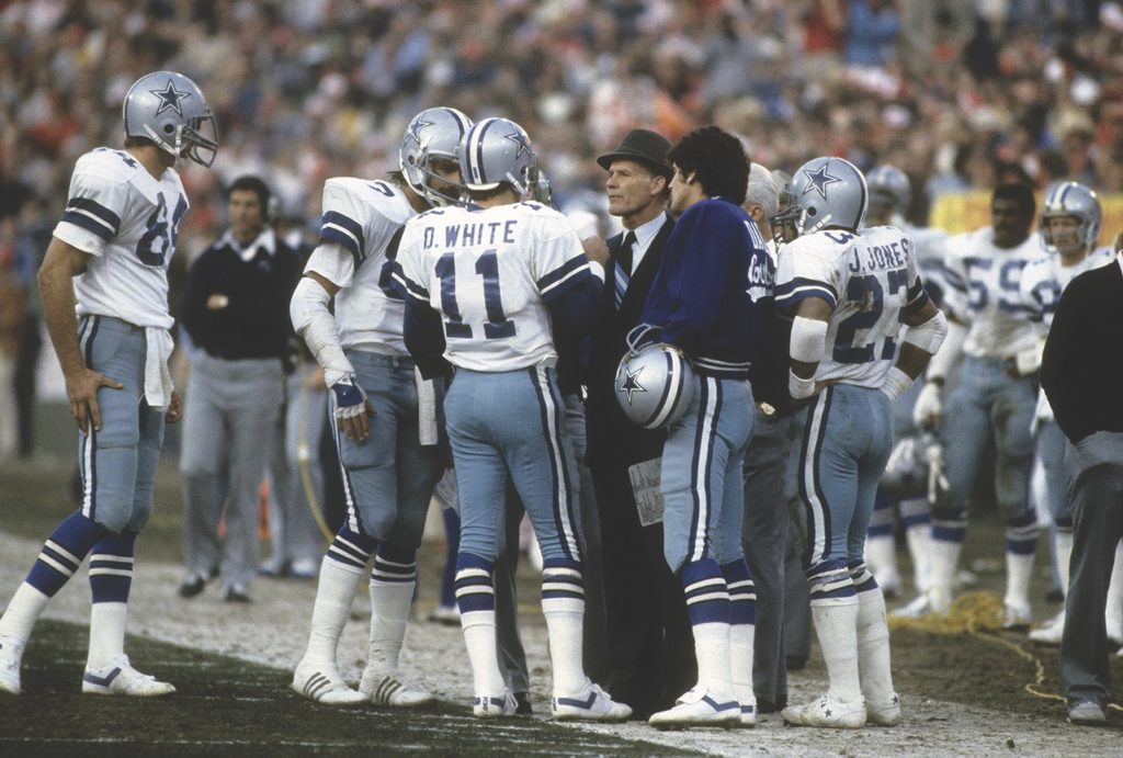 When Landry was the Cowboys’ coach (top, in 1980), his fedora became an ever-present signature. Following his death from leukemia in 2000, Cowboys players including quarterback Troy Aikman (bottom) donned jerseys emblazoned with miniature hats in Landry’s memory. (Focus on Sport/Getty Images)