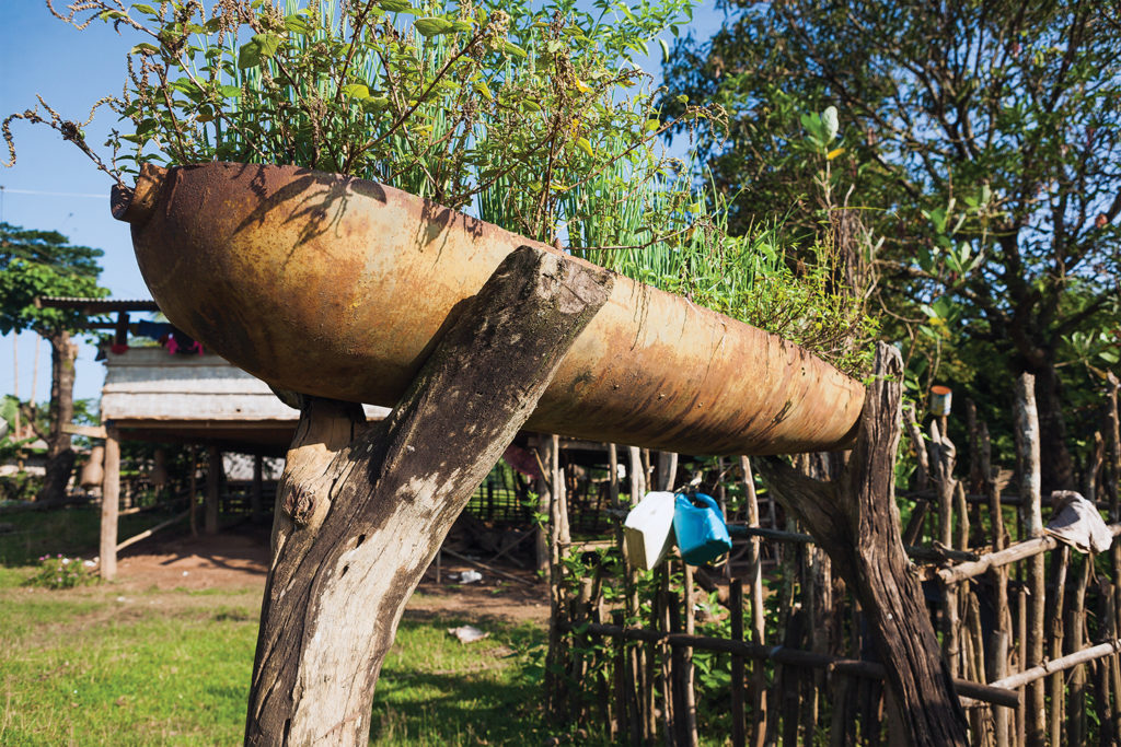 Photo of a cluster bomb cannister has been recycled and used as a planter. These cannisters split in half when released from the aircraft, unleashing hundreds of explosive 'bomblets'. A very common sight in the smaller villages of Laos.
