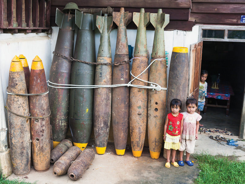 Photo of defused UXO outside a house in Xieng Khouang. Over 30% of the bombs dropped on Laos by the US failed to explode - leaving literally millions of items of ordinance (many of them tiny mine bomblets from cluster bombs) sitting in villages, buried in rice padddies, and scattered over the hillsides. Casualties from UXO are estimated at 12,000 since 1973. A substantial industry in scrap metal has arisen from the abundance of recoverable (but still fused) bombs, both due to its relative lucrativeness (compared with growning rice), and also out of desperation, as thousands of hectares of land has been rendered unfarmable until cleared of UXO. Once defused, much of this war scrap is also put to practical use; cluster bomb casings are used as planters and house stilts, bomb cases for fencing and jettisoned fuel tanks converted into fishing boats.