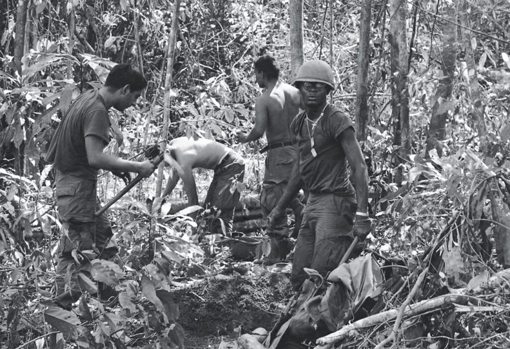 Photo of men in the 4th Infantry Division clearing a landing zone for helicopters amid the dense foliage of the Central Highlands in 1967.