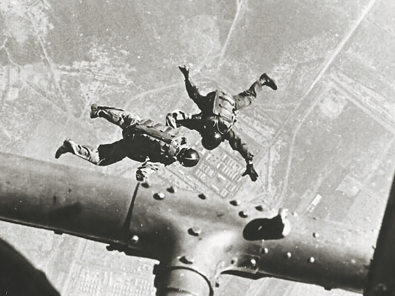 Photo of HALO parachutists of SOG link up beneath a Huey helicopter above Camp Long Thanh.