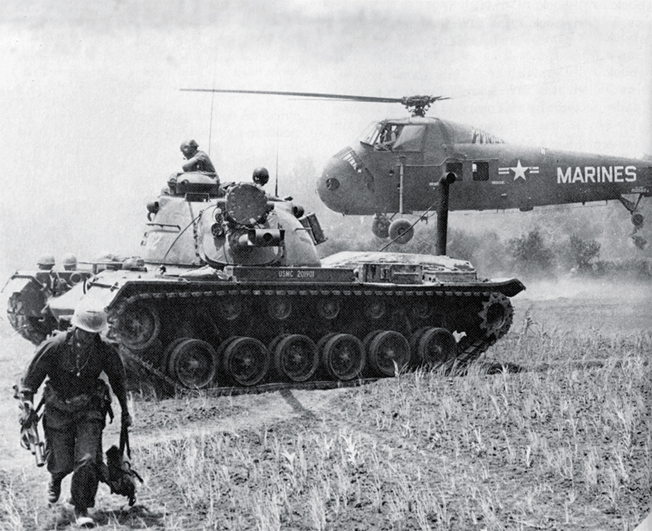 Photo of a MAG-16 helicopter evacuating STARLITE casualties, while a Marine M-48 tank stands guard. The Marine on the left carries a M-79 grenade launcher.