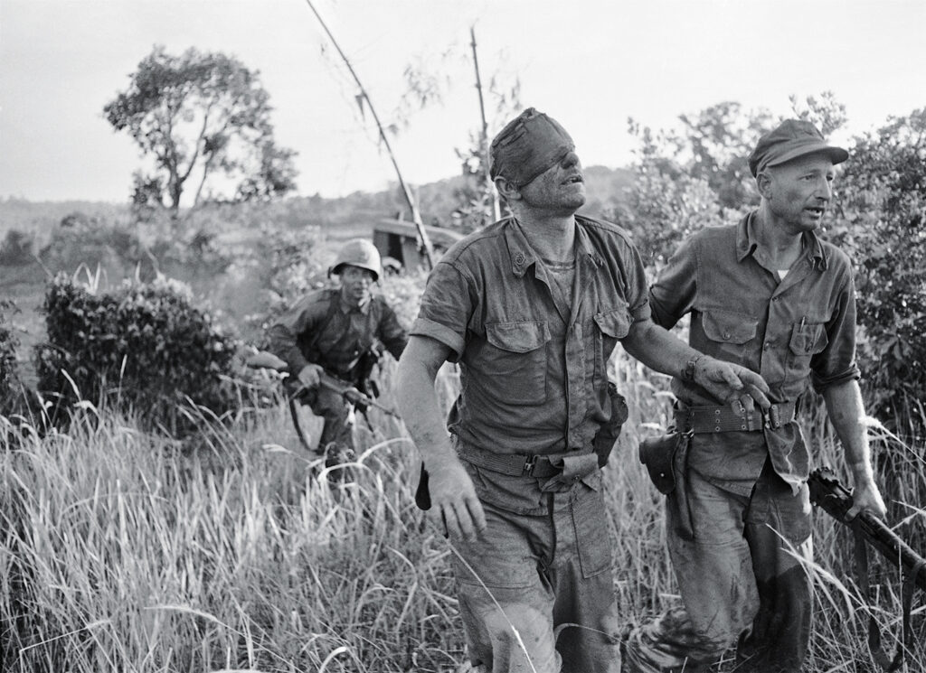 Photo of a U.S. Marine who was wounded in the head as he fought against the Viet Cong from inside an amphibious tank, is led to an evacuation helicopter landing zone at Van Tuong, Vietnam. More than two bitter decades of war in Vietnam ended with the last days of April 1975. Today, 40 years later, Arnett has written a new memoir, “Saigon Has Fallen,” detailing his experience covering the war for The Associated Press.