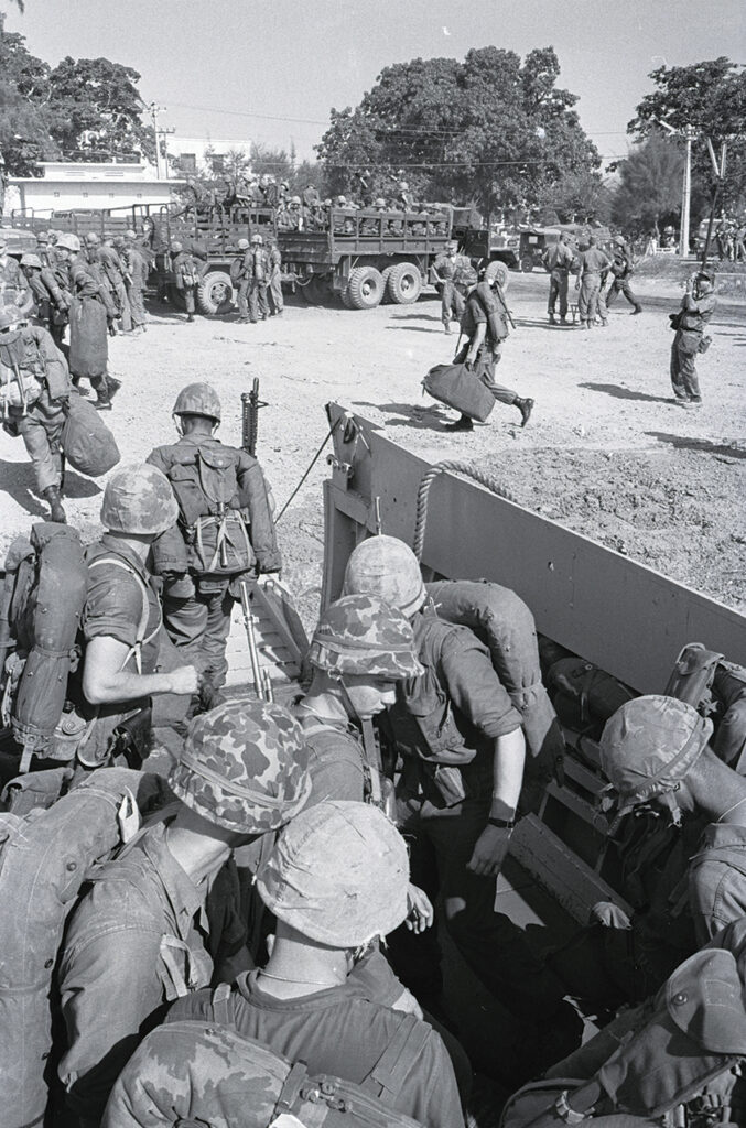 Photo of trucks with U.S. Marines are loaded, ready to take the fighting men to their camp, as others pour off landing craft Aug. 14. Within a week they were engaged in a battle with Viet Cong guerrillas, which ended in one of the worst beatings ever suffered by the Viet Cong.