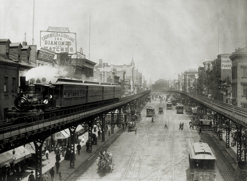 Photo of elevated trains rolling over busy streets in Manhattan's Bowery neighborhood.
