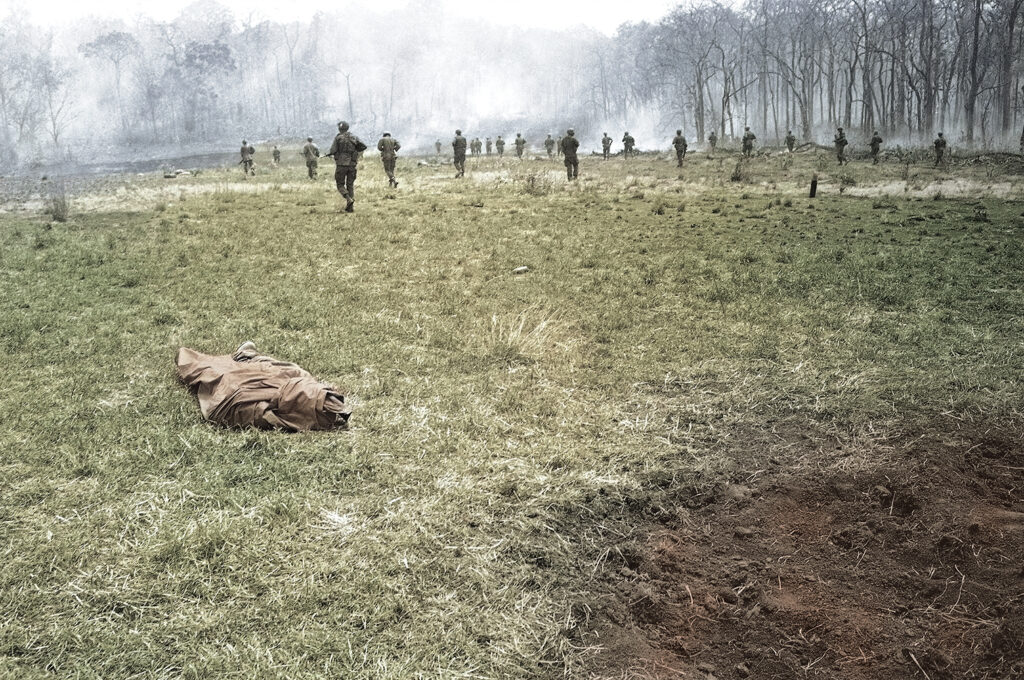 Photo of Infantrymen of the U.S. 4th Division move across clearing passing poncho-wrapped body of a buddy at the spot where he fell in Vietnam on March 23, 1967. Action took place 20 miles northwest of Pleiku in the central highlands of Vietnam, near the Cambodian border.