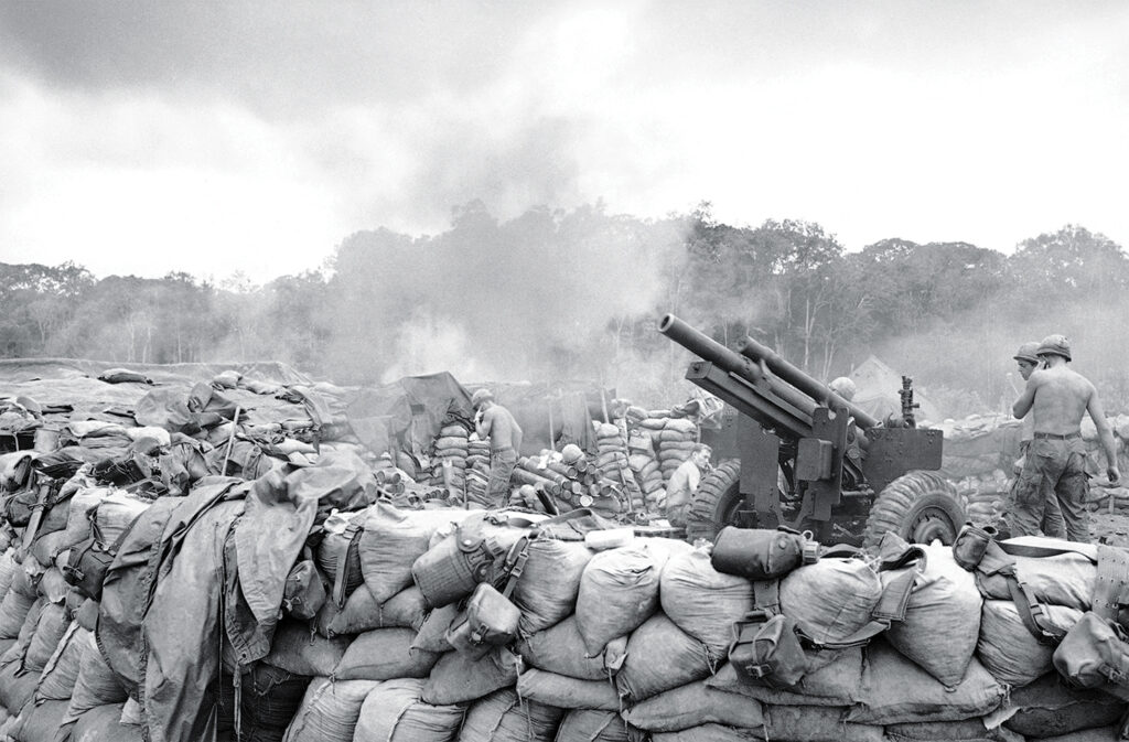 Photo of U.S. artillerymen firing 105mm Howitzer rounds in support of a 4th division operation near the Cambodian border in Vietnam on July 17, 1967. The artillery pieces are set into sandbag emplacements at a forward camp operated by the division.