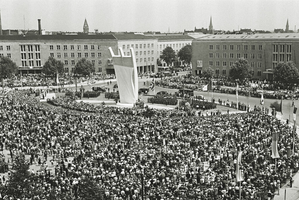 Photo of West Berliners gathering on Platz der Luftbrücke outside Berlin’s Tempelhof Field to dedicate the Berlin Airlift Memorial.