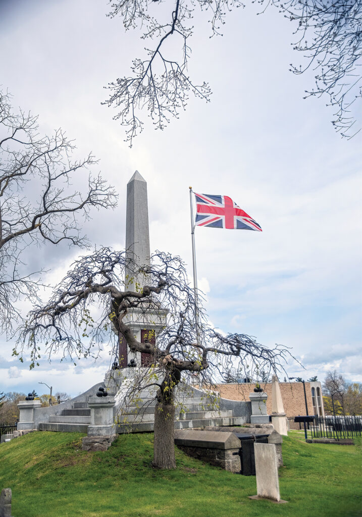 Photo of a tall gravestone is accompanied by a British flag, waving in the wind, in Drummond Hill Cemetery in Niagara Falls, Ontario.