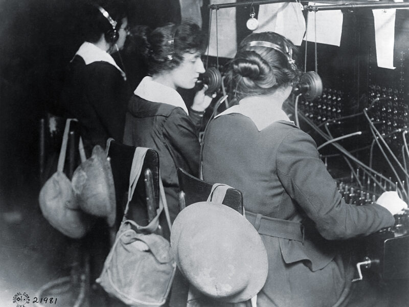 Photo of Telephone operators working with the U.S. Signal Corps work at a switchboard in American military headquarters at St.-Mihiel, France. Gas masks and helmets hang at the ready in case of German shelling or gas attacks. Their efficiency and bravery contributed greatly to the effort to capture St.-Mihiel.