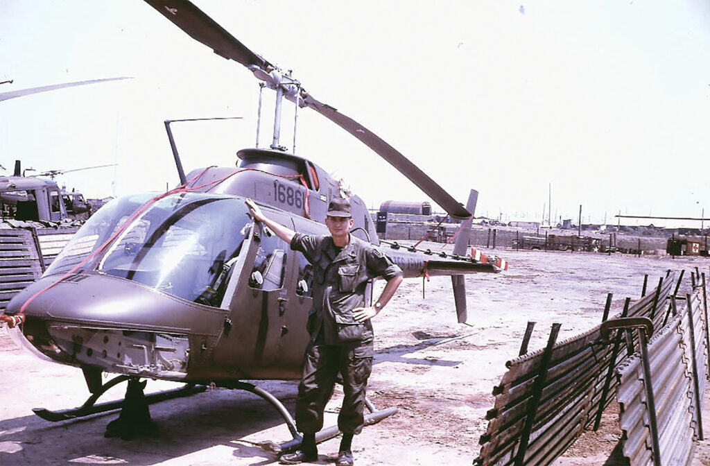 Photo of David L. Anderson standing next to a Bell OH-58 Kiowa helicopter.