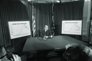 Photo of President Nixon flanked by charts he used to illustrate his televised speech from the White House 4/7 in which he announced he will withdraw an additional 100,000 U.S. troops by December 1. The charts show the authorized troops level in South Vietnam.