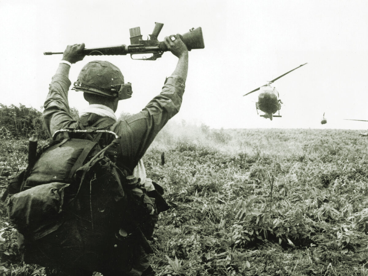 Photo of a soldier in the U.S. Army 1st Air Cavalry holds his rifle above his head as he serves as a 'traffic cop' for helicopters landing in a field during an operation north of Saigon in the Vietnam War, South Vietnam. The helicopters were bringing members of the unit to the area that they were to patrol.
