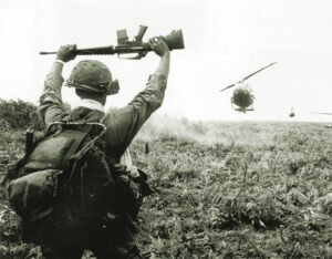 Photo of a soldier in the U.S. Army 1st Air Cavalry holds his rifle above his head as he serves as a 'traffic cop' for helicopters landing in a field during an operation north of Saigon in the Vietnam War, South Vietnam. The helicopters were bringing members of the unit to the area that they were to patrol.