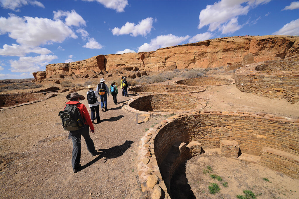 CHACO CULTURE NATIONAL HISTORICAL PARK, NM - MARCH 23, 2014: A guide leads a group of visitors through past excavated circular kivas in the ruins of a massive stone complex (Chetro Ketl) at Chaco Culture National Historical Park in Northwestern New Mexico. The communal stone buildings were built between the mid-800s and 1100 AD by Ancient Pueblo Peoples (Anasazi) whose descendants are modern Southwest Indians. Chaco was a major center of Ancestral Puebloan culture for more than 1,000 years.