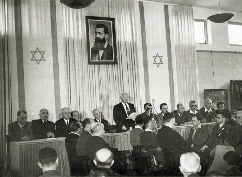 Photo of el Aviv, Israel- Members of the newly created state of Israel gathered to hear Prime Minister David Ben Gurion read the Jewish "Declaration of Independence." Left to right: Baruch Schitrit, Minister of Arab Affairs and Police; David Remez, Minister of Communications; Felix Rosenblueht, Minister of Justice; Fritz Bernstein, Minister of Trade; Rabbi Juda Fishman of Jerusalem; David Ben Gurion, Prime Minister and Defense Minister; Moshe Shapiro, Minister of Immigration; Moshe Shertock, Minister of Foreign Affairs; Eliazar Kaplan, Minister of the Treasury; M. Ben Tov, Minister of Labor; and A. Zisling, Minister of Agriculture.