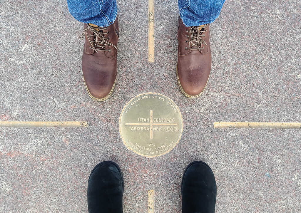 Photo of 2 sets of booted feet standing at the famous 4 Corners of the USA. The 4 corner states are Colorado, Utah, Arizona and New Mexico where all 4 states meet in one spot.