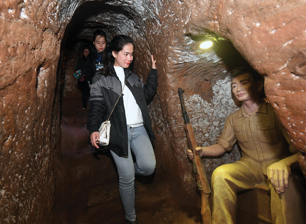 In this picture taken on January 18, 2018, a guide walks past a concrete model of a militia member (R) inside the Vinh Moc tunnel network, at the Vinh Moc commune in the central coastal province of Quang Tri. The Vinh Moc tunnels are among thousands of underground passageways built across Vietnam throughout the war, including the massive Cu Chi tunnels in Saigon, where Viet Cong guerrillas took shelter beneath the former Southern capital, which was renamed Ho Chi Minh city after the war's end in 1975.