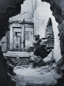 Photo showing The long awaited all out Arab attack on the Jews has begun according to widespread reports of violence and attacks from the Holy Land. Here we see two members of the Palmach, the striking force of the Haganah, as they fired through a hole in a wall while training recently for city fighting. The Haganah, once illegal, is now working openly and has registered all men and women between the ages of 17 and 35. Actually, those under 25 only are called in the draft. The main problem has been to keep too many men and women over 35 from trying to serve when they are of more use in vital civilian jobs. The Defense Army organized 30 years ago has since grown to a full and efficient fighting force capable of coping with the dangerous situation which now faces it.