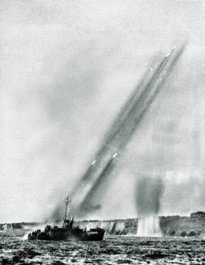 Photo of a U.S. landing craft fires rocket projectiles at the rugged shore of Iwo Jima in a pre-invasion bombardment, Feb. 19, 1945. Four rockets trailing smoke can be seen zooming into the air. This photo was made from another landing craft before the Marines stormed ashore.