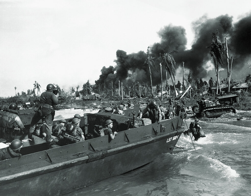 Photo of Australian troops storm ashore in the first assault wave to hit Balikpapan on the southeast coast of oil-rich Borneo. A Coast Guard Combat Photographer stands in the landing craft. July 1945.