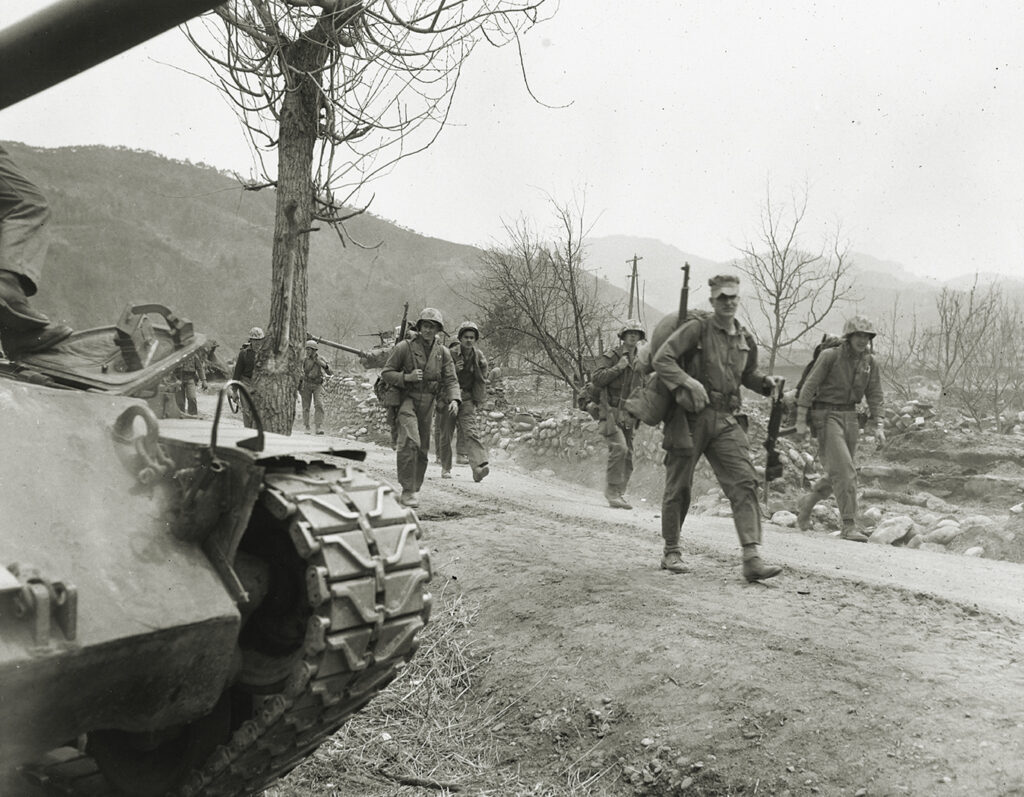 Photo of U.S. Marines passing through a village during the Korean War.