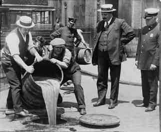 New York City Deputy Police Commissioner John A. Leach (right) watches as Prohibition agents pour illegal liquor into a sewer in 1921.