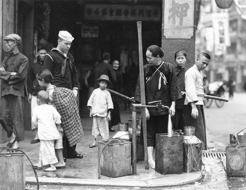 A U.S. sailor observes a woman filling tubs at a public well in Hong Kong in 1931. (National Archives)